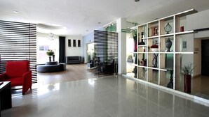 Un hall d’entrée moderne avec un fauteuil rouge, un canapé noir et une vitrine contenant des objets décoratifs.