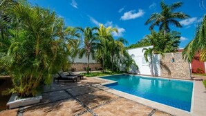 A swimming pool surrounded by palm trees and a stone wall, with lounge chairs and a tiled patio area. - Refreshing Double Room Retreat with Poolside Access & Relaxing Terrace in Mérida (Mérida)
