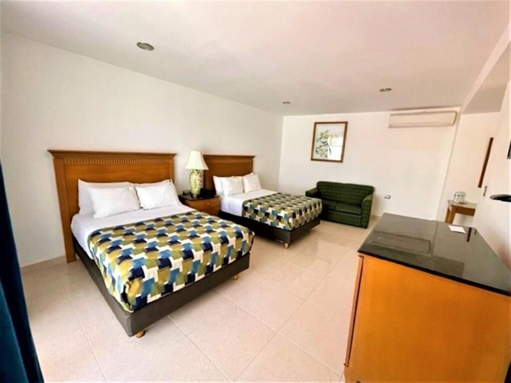 A hotel room with a large bed, a smaller bed, a green sofa, a desk, and a lamp.