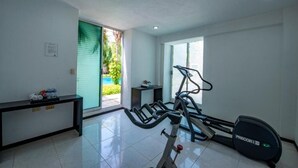 A home gym with a treadmill, elliptical, and weights, a small table with towels, and a window with a view of greenery. - Refreshing Double Room Retreat with Poolside Access & Relaxing Terrace in Mérida (Mérida)