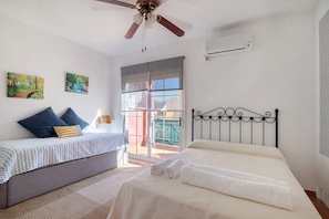 Een slaapkamer met een bed, een plafondventilator, een raam en een deur die uitkomt op een balkon.