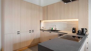 A modern kitchen with light wood cabinetry, a black countertop, and a built-in stove.