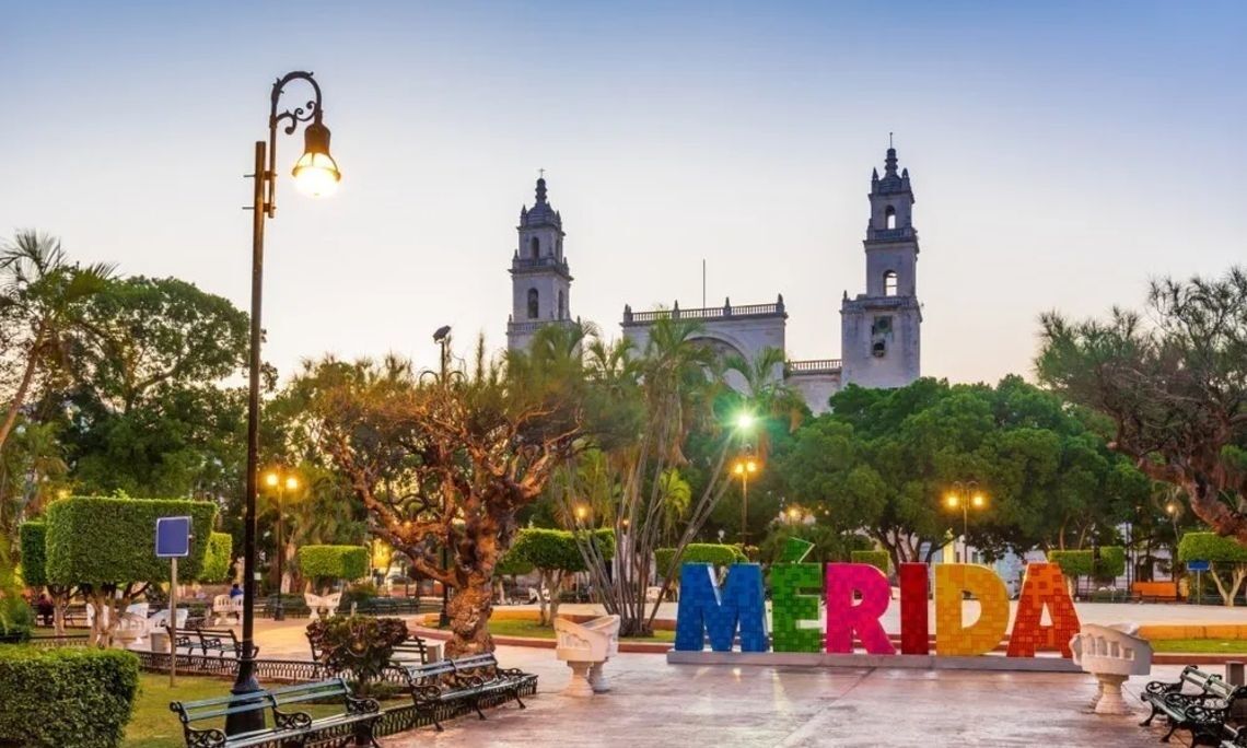 A plaza with a large sign spelling "MERIDA" and two prominent towers in the background.