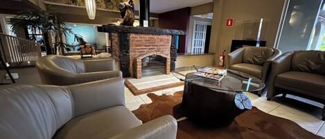 A modern living room with leather sofas, a glass coffee table, a fireplace, and a large window.