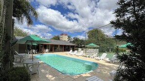 A swimming pool with lounge chairs and umbrellas, surrounded by a fence and trees. - Nature Retreat Suite Surrounded by Canyons, Waterfalls, and Miles of Scenic View (Paraná)