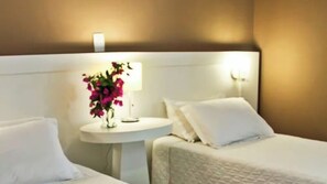 Habitación de hotel con dos camas, una mesita de noche con lámpara e iluminación en la pared.