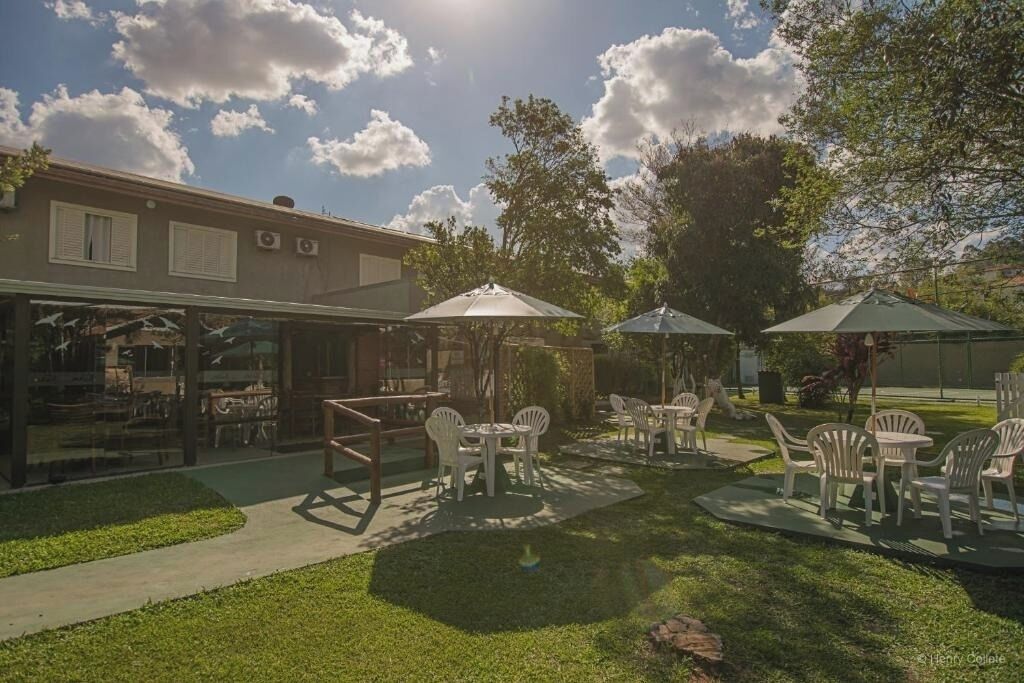 An outdoor patio area with tables and chairs, surrounded by a building with large windows and a garden.