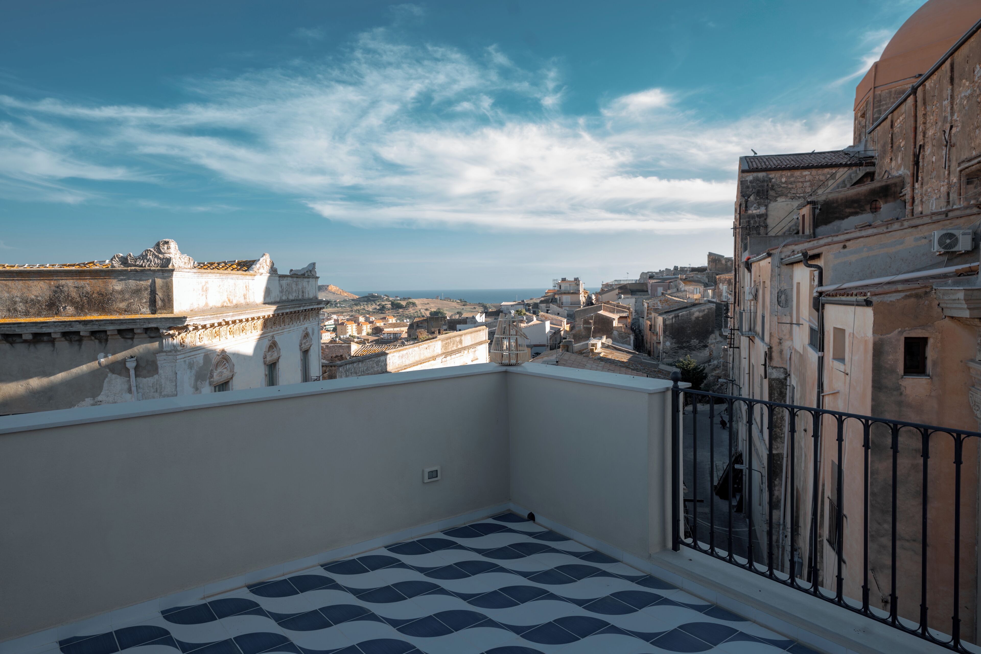 A rooftop terrace with a patterned floor, a metal railing, and a view of a cityscape with historical buildings.