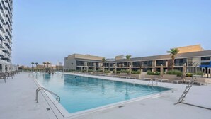 A swimming pool area with lounge chairs and umbrellas, surrounded by modern buildings. - JVC Sleeps 4 With Amazing Views and Large Balcony (Dubai)