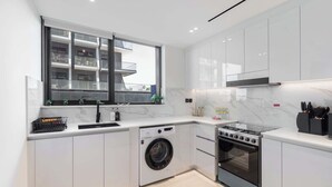 A modern kitchen with white cabinets, a built-in washing machine, a stove, and a window overlooking a balcony. - JVC Sleeps 4 With Amazing Views and Large Balcony (Dubai)