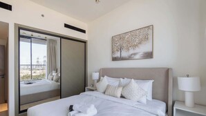A hotel room with a bed, a nightstand, a lamp, a painting, and a sliding door with a view. - JVC Sleeps 4 With Amazing Views and Large Balcony (Dubai)