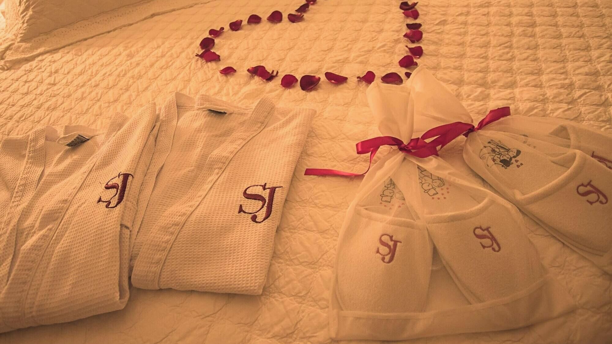 A bed with neatly folded white robes and towels, each with embroidered initials.