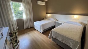 Habitación de hotel con dos camas, una ventana con cortinas, un equipo de aire acondicionado y una mesita de noche con lámpara.
