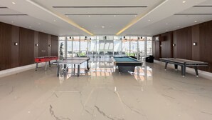 Un vaste espace de loisirs intérieur comprenant une table de billard, un baby-foot et une table de ping-pong.