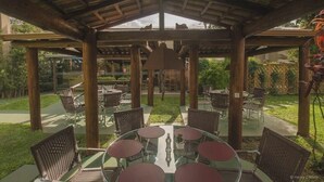 An outdoor patio with round tables and chairs, a wooden pergola structure, and a view of the surrounding greenery.