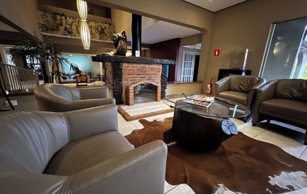 A modern living room with leather sofas, a glass coffee table, a fireplace, and a large window.