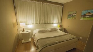 A hotel room with a bed, bedside table, lamp, and curtains.