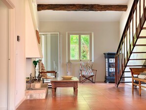 A spacious room with a wooden table, a chair, a window with a view of greenery, and a staircase.