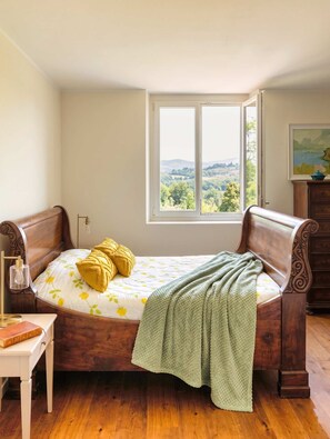 Een slaapkamer met een houten bed, uitzicht op het landschap, een nachtkastje met een lamp en een dressoir.