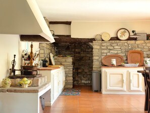 A kitchen with stone walls, a wooden beam ceiling, and a tiled floor.
