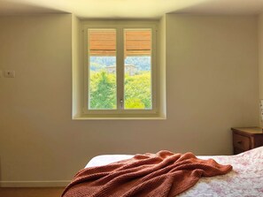 A bedroom with a window, a bed, and a nightstand.