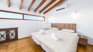 A modern bedroom with a large bed, wooden beams, an air conditioning unit, and a view through a window. - Luz del Faro, apartment in historic townhouse with sea view - by OYOOSTAYS (La Vila Joiosa)