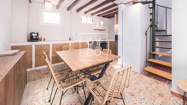 A modern kitchen with a wooden table and chairs, a white cabinet, and a staircase. - Luz del Faro, apartment in historic townhouse with sea view - by OYOOSTAYS (La Vila Joiosa)