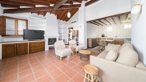 A spacious living area with a fireplace, a television, and a dining area with chairs and a table. - Luz del Faro, apartment in historic townhouse with sea view - by OYOOSTAYS (La Vila Joiosa)