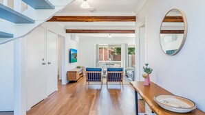 Un interior moderno con una escalera de madera, una zona de comedor con un banco y sillas, y un espejo grande en la pared.