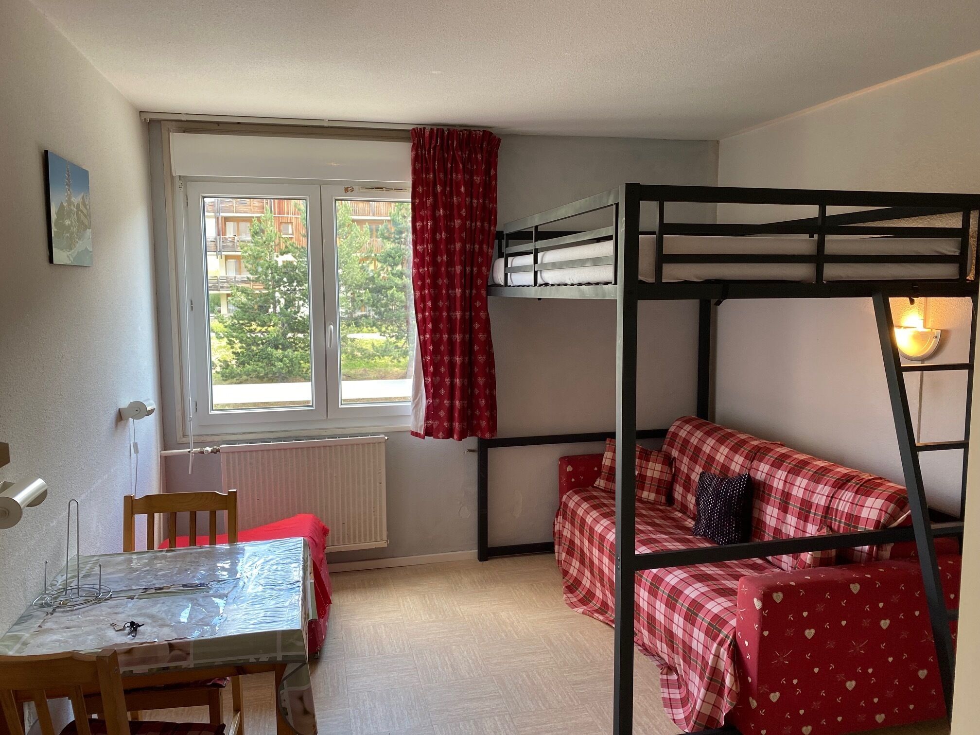Une pièce avec des lits superposés, une table avec des chaises, une fenêtre avec des rideaux et un radiateur.