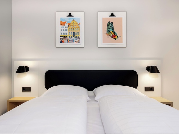 A hotel room with a bed, two wall-mounted lamps, and two framed pictures on the wall.