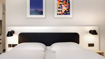 Ein Hotelzimmer mit einem großen Bett, zwei Wandlampen und zwei gerahmten Kunstwerken darüber.