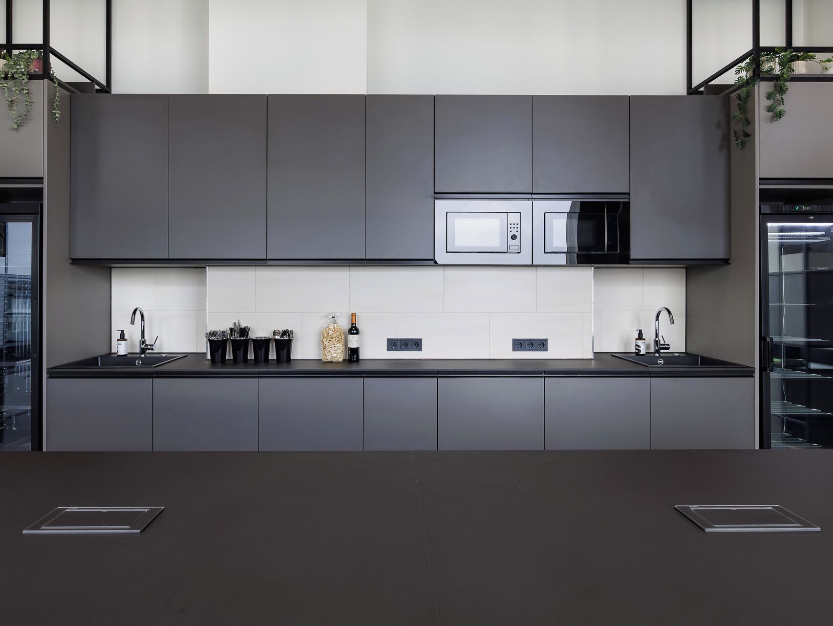 Une cuisine moderne avec des meubles de couleur sombre, un îlot central, un four à micro-ondes et une bouteille de vin.