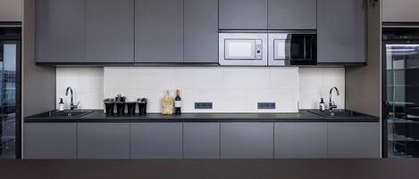 A modern kitchen with dark cabinetry, a central island, a microwave, and a wine bottle.