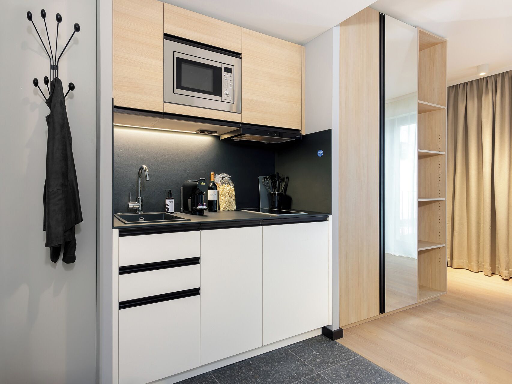 A modern kitchen with a built-in microwave, a sink, and a wine bottle.