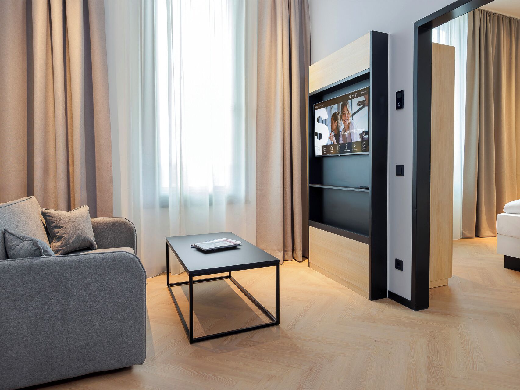 Ein modernes Wohnzimmer mit einem grauen Sofa, einem Couchtisch und einem an der Wand befestigten Fernseher.