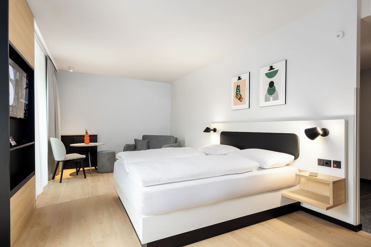 Una habitación de hotel moderna con una cama grande, un escritorio con silla y dos obras de arte colgadas en la pared.