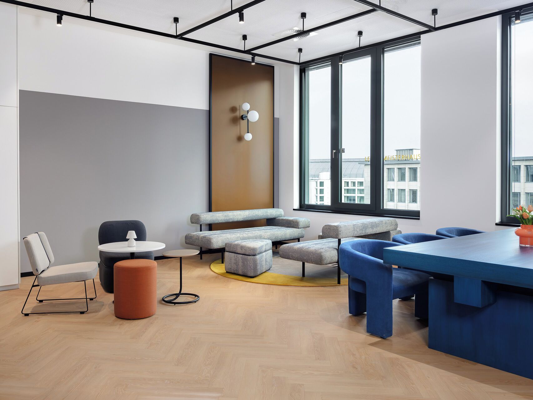 Un espacio de oficina moderno con una gran mesa, diversas opciones de asiento y amplios ventanales con vistas a la ciudad.
