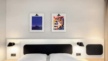 A hotel room with a bed, two wall-mounted lamps, and two framed artworks.