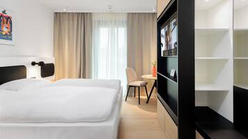 A modern hotel room with a large bed, a desk, a chair, and a TV on the wall.