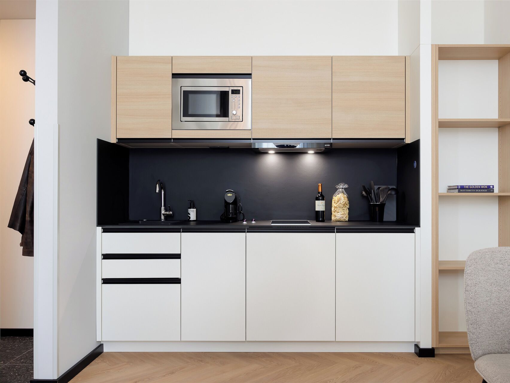 A modern kitchen with a built-in microwave, a coffee maker, and a wine bottle on the counter.