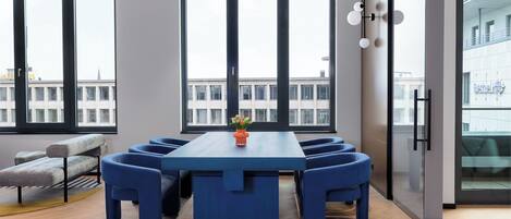 Una sala de conferencias moderna con una larga mesa, sillas azules y un jarrón de flores.