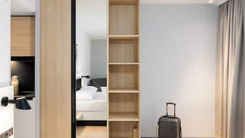 A hotel room with a sliding closet, a bed, a desk, a suitcase, and a view of the hallway.