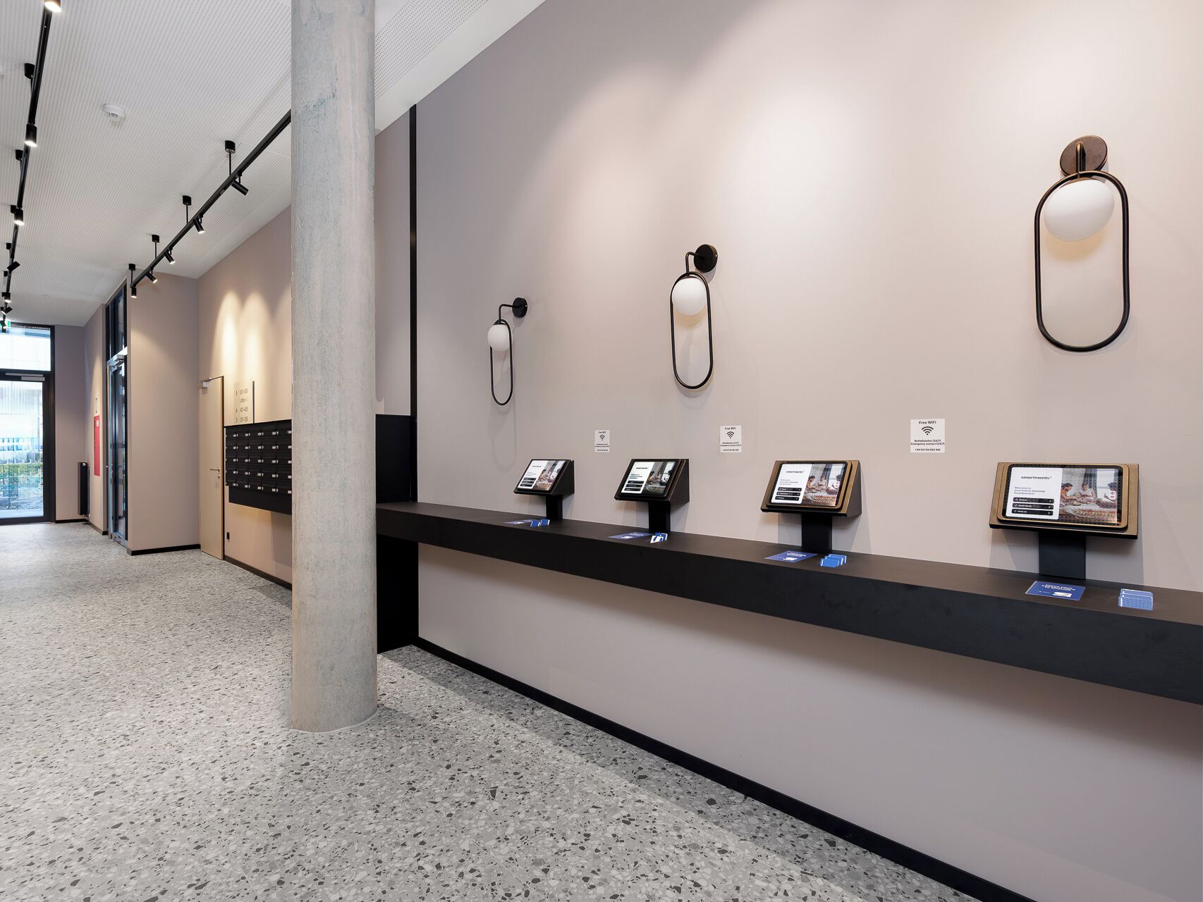 Un hall d’hôtel moderne avec un comptoir d’accueil, des bornes d’information et une grande colonne.