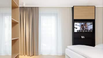 Ein modernes Hotelzimmer mit einem Bett, einem an der Wand befestigten Fernseher und einem Holzschrank.