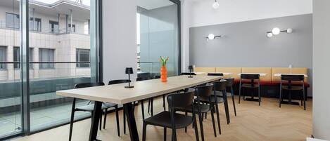Ein moderner Konferenzraum mit großem Tisch, Stühlen und einer Glaswand, die einen Blick auf die Außenansicht des Gebäudes bietet.