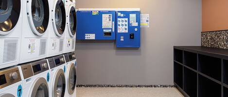 A laundry room with multiple washing machines, a blue utility box, and a tiled floor.