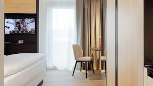 A modern hotel room with a bed, a TV mounted on the wall, a small table with a vase, and a chair.