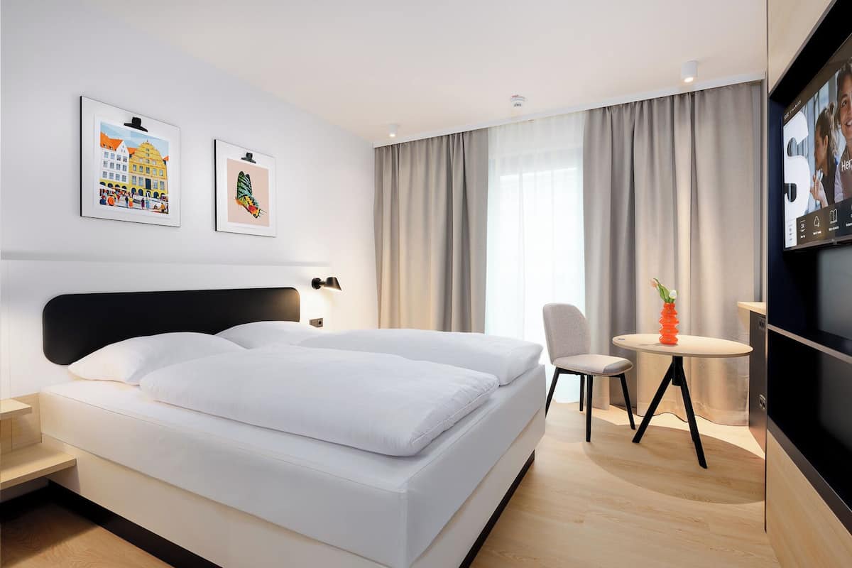 Una habitación de hotel moderna con una cama grande, un escritorio y un televisor.
