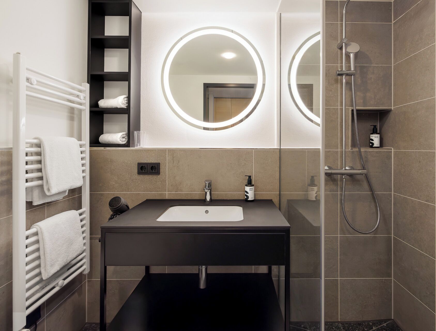 A modern bathroom with a black sink, two mirrors, a towel rack, and a shower.